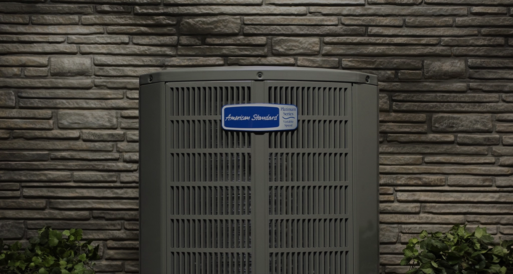 American Standard outdoor AC unit installed against a stone wall